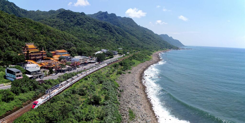 Puyuma Express train dashing along the coast between forested mountains and the blue Pacific Ocean in Toucheng Yilan